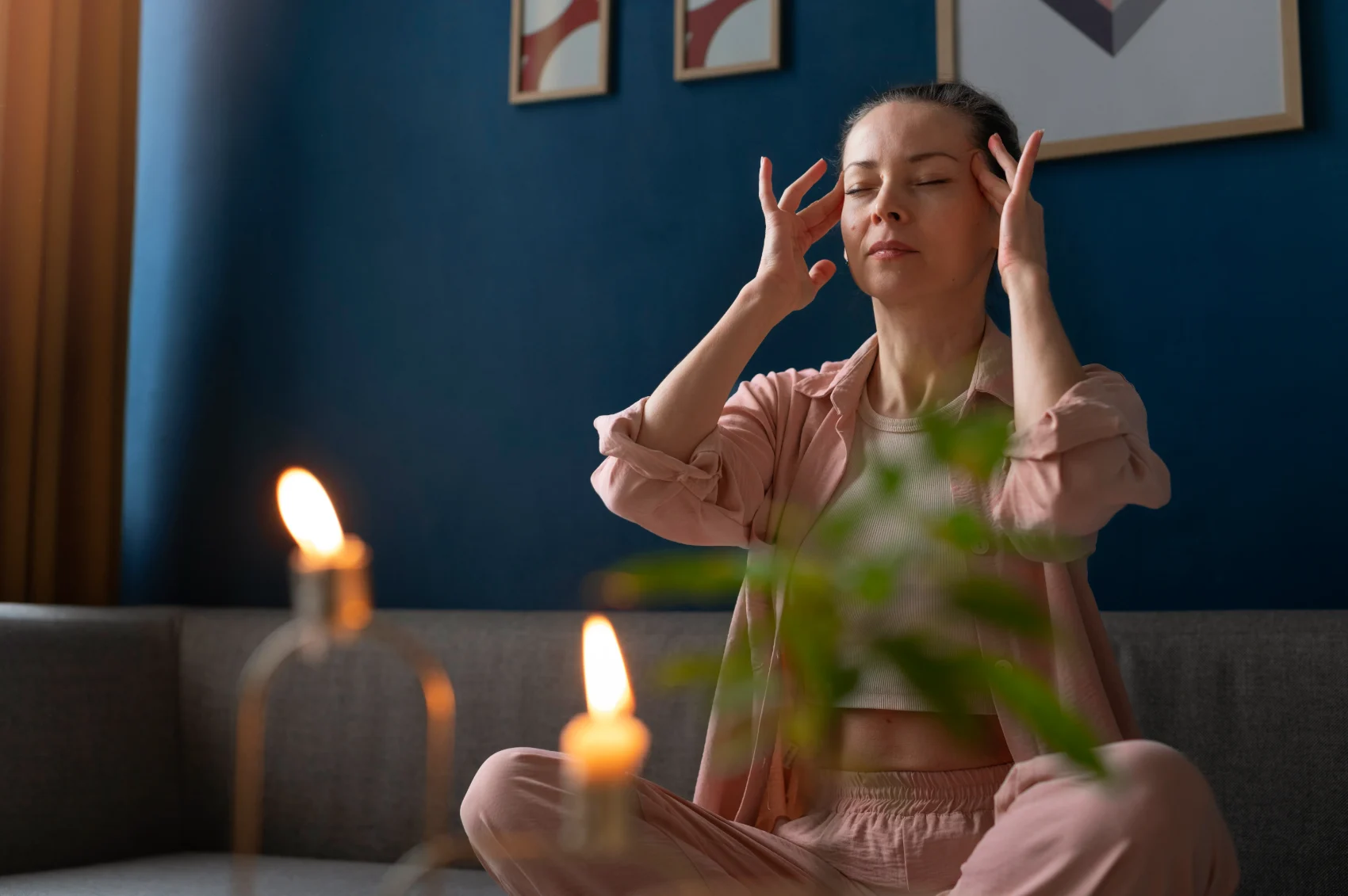 A person sitting calmly with eyes closed and hands at the temples in a warmly lit room, taking a quiet moment of inward reflection