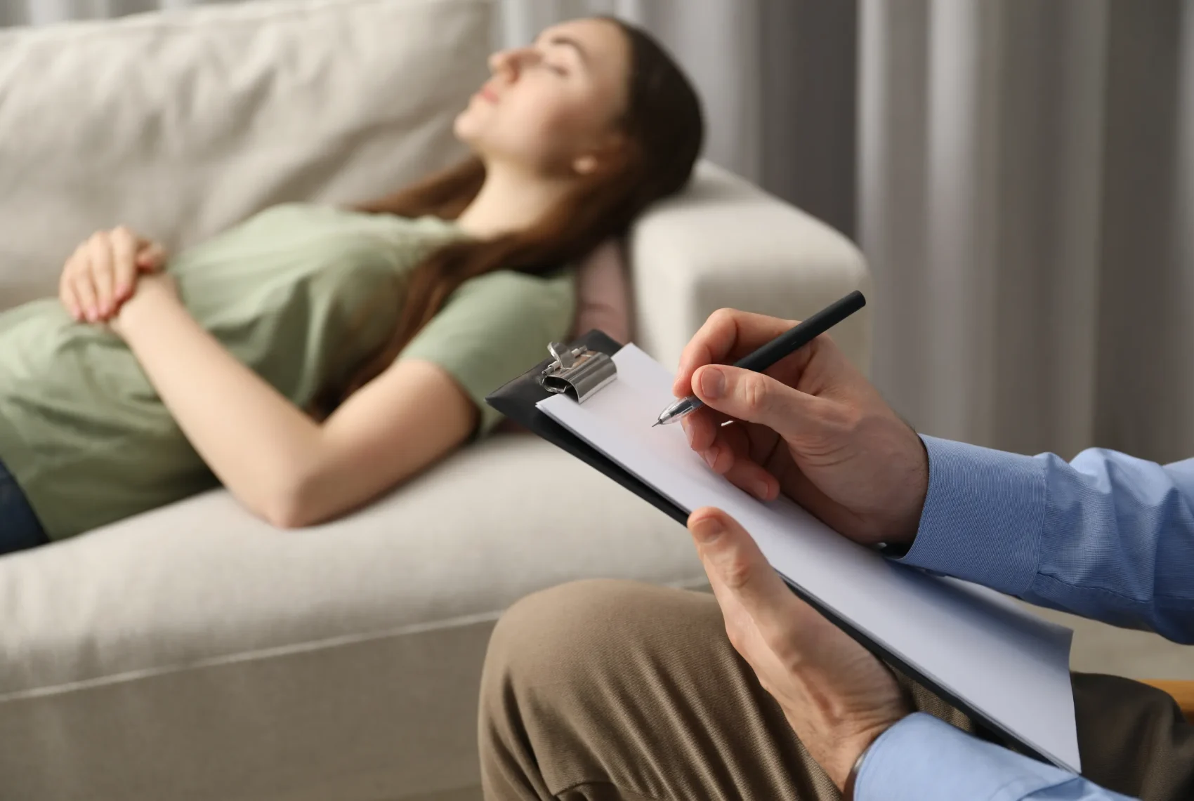 A practitioner writing notes on a clipboard while a client rests comfortably during a therapy session